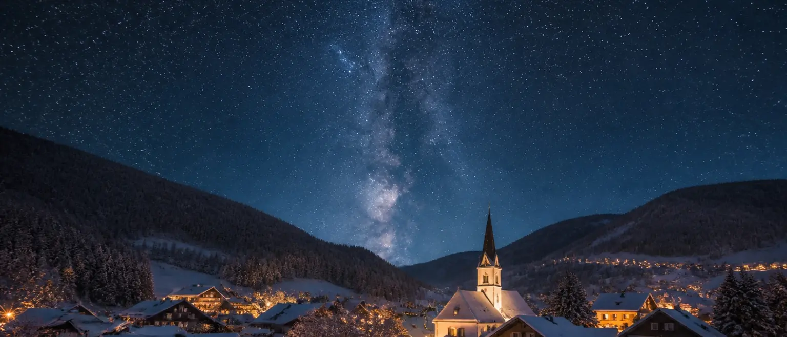 Sternenhimmel mit Milchstraße über einem verschneiten Dorf mit Kirche.